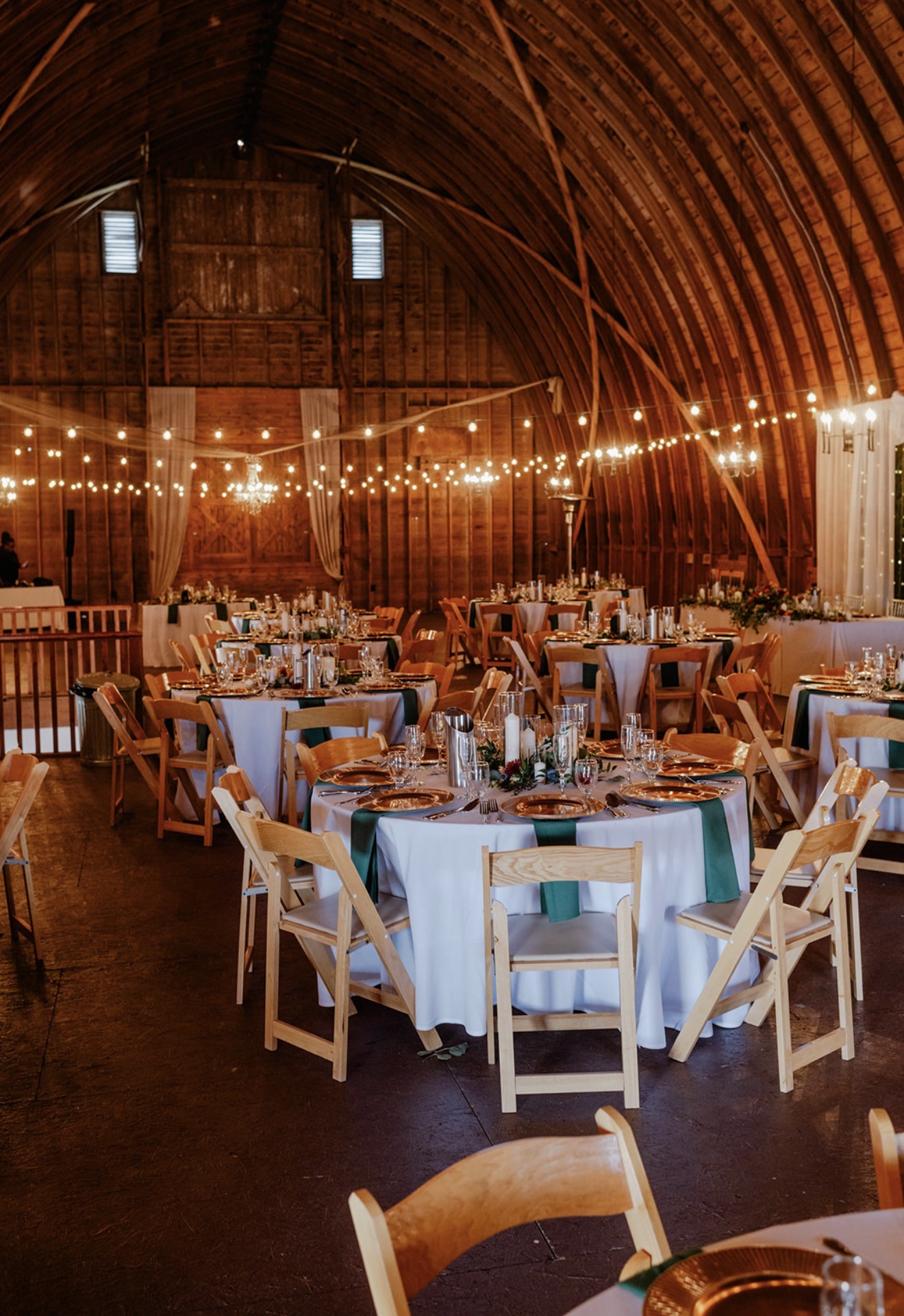 The barn set for dinner in daylight with teal linens and round tables.