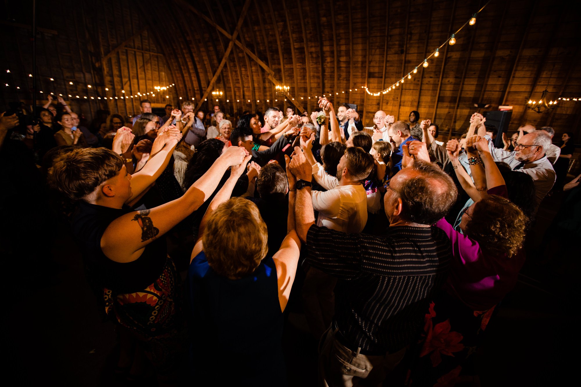 Packed dance floor in the barn under warm string lights
