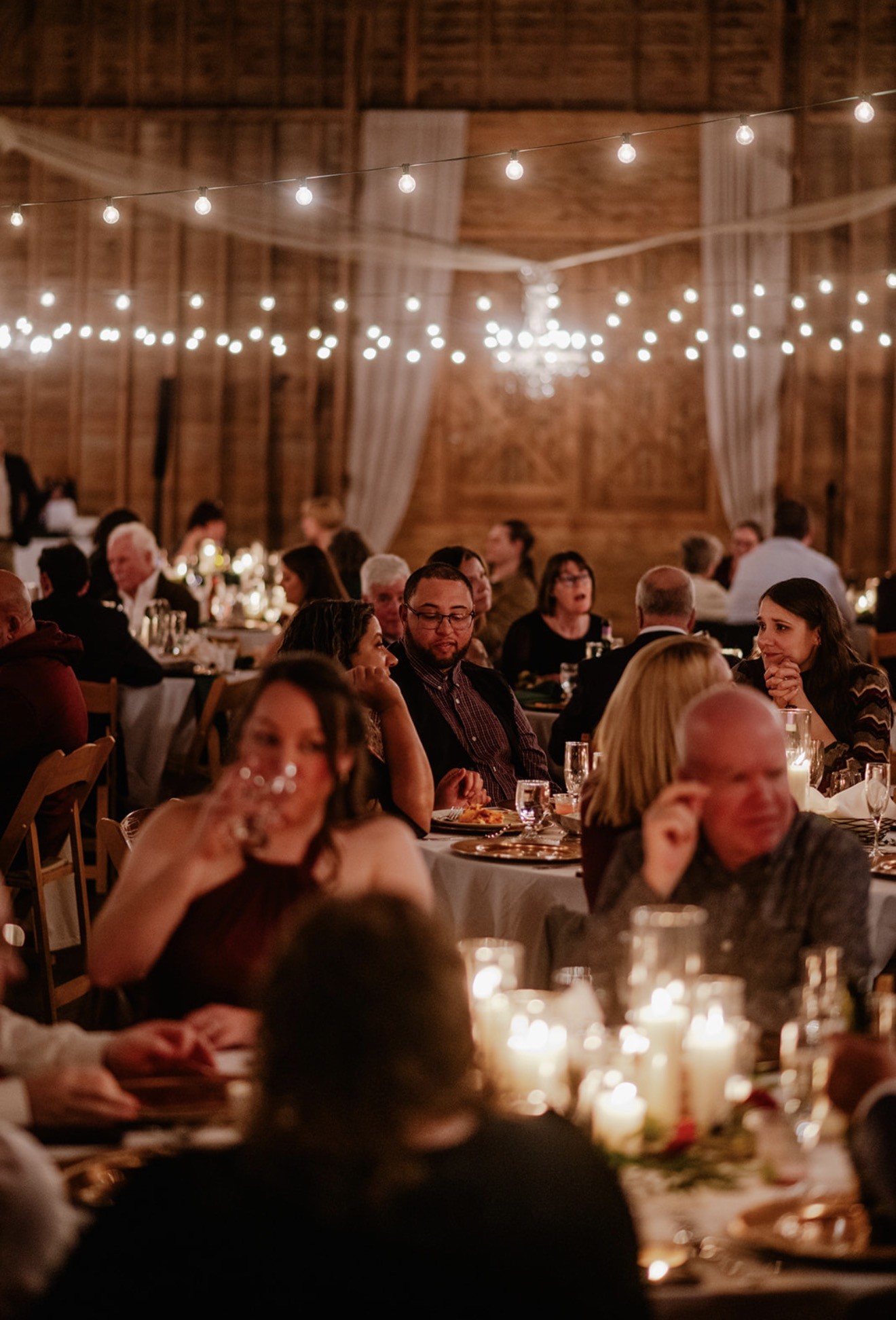 Guests at dinner in the barn by candlelight and hanging bulbs.