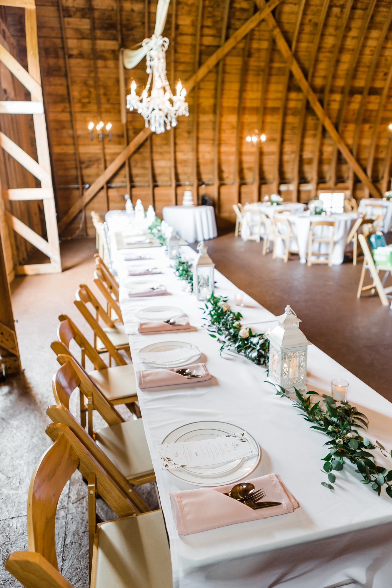 The head table set for dinner beneath a chandelier in the barn
