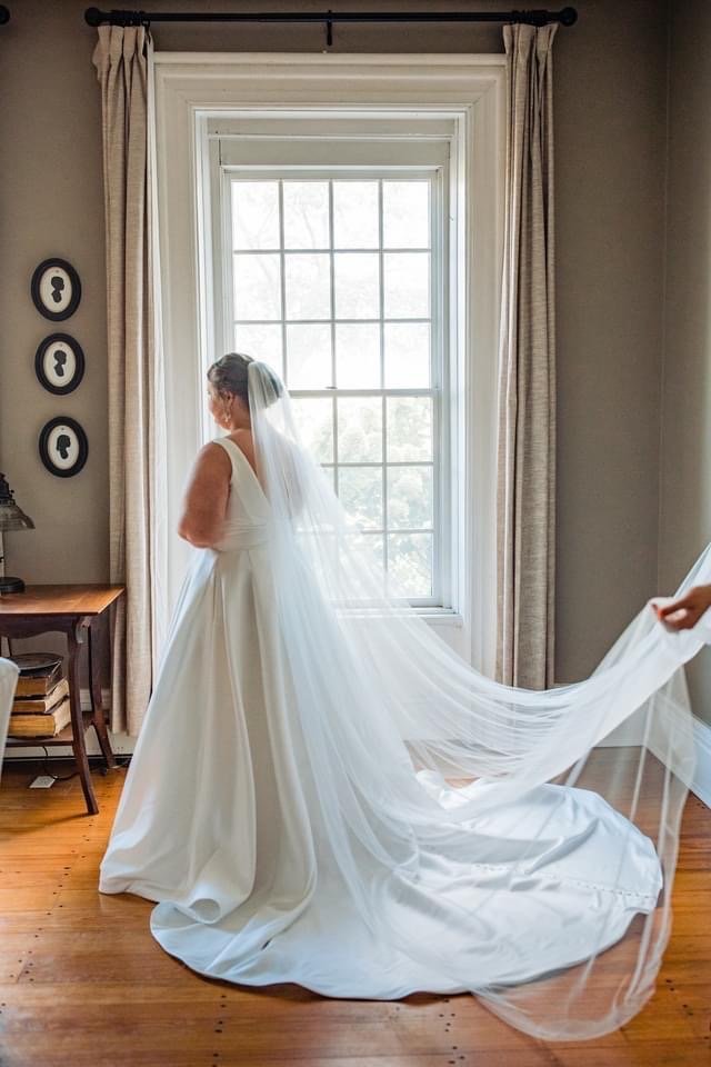 A bride stands in a farmhouse doorway in her gown.
