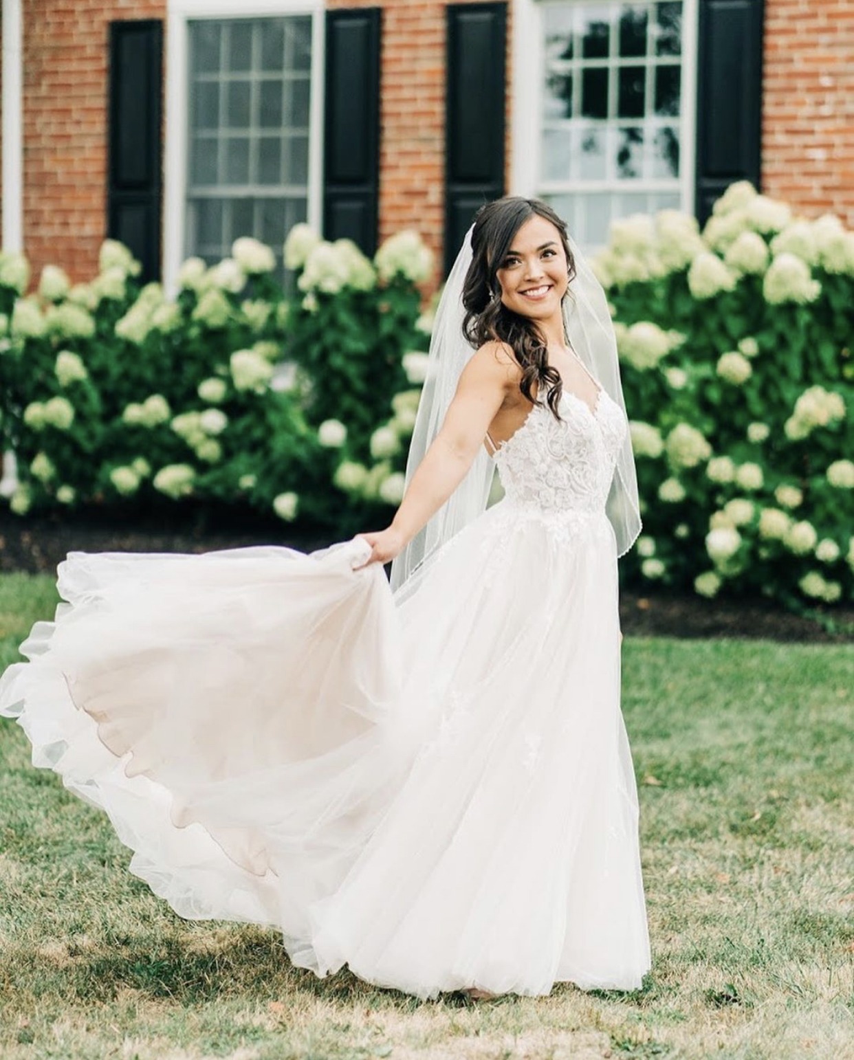 A bride turning in her gown beside the farmhouse hydrangeas.