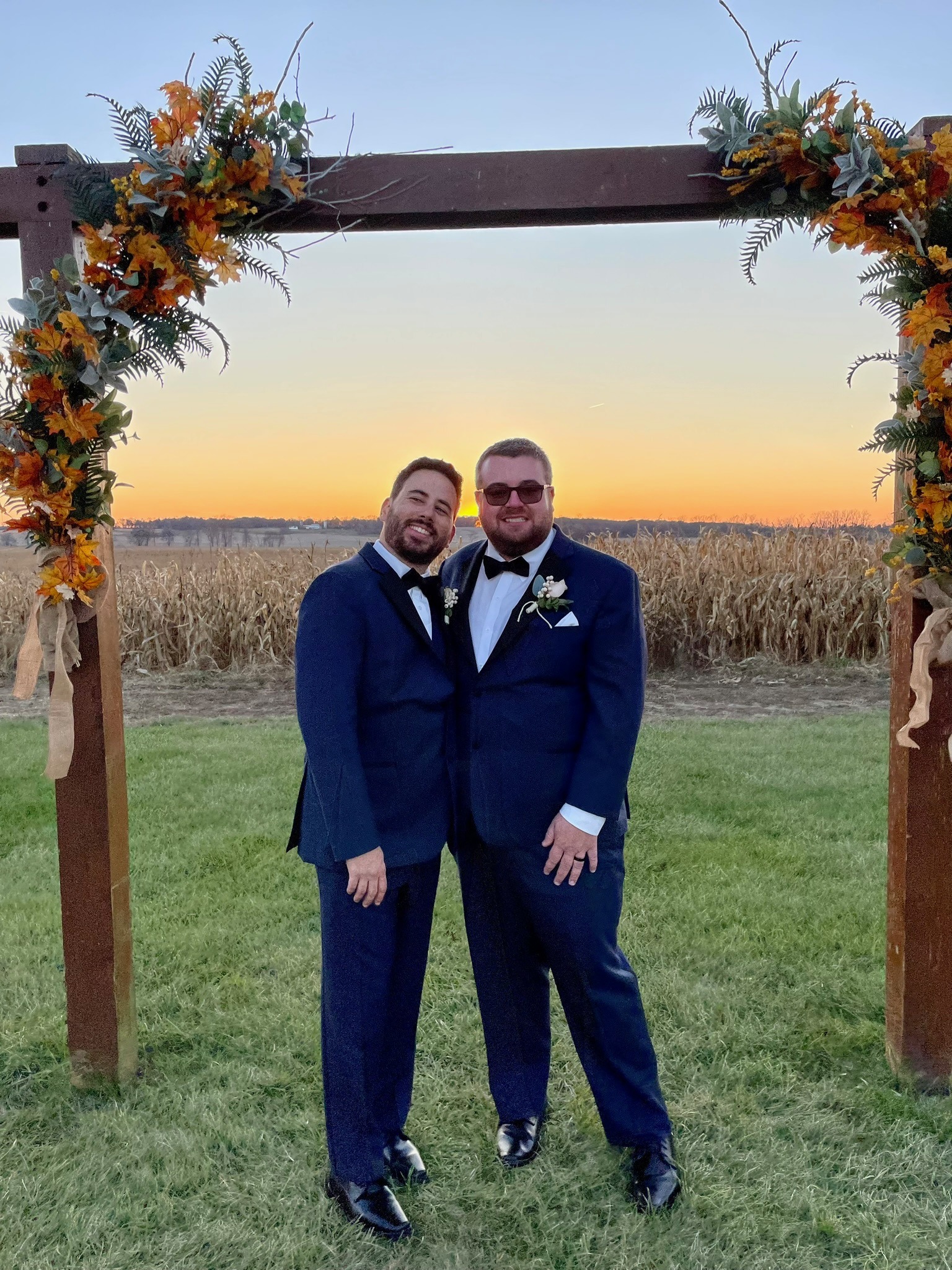 A couple under the autumn arch at sunset with the cornfield behind them.