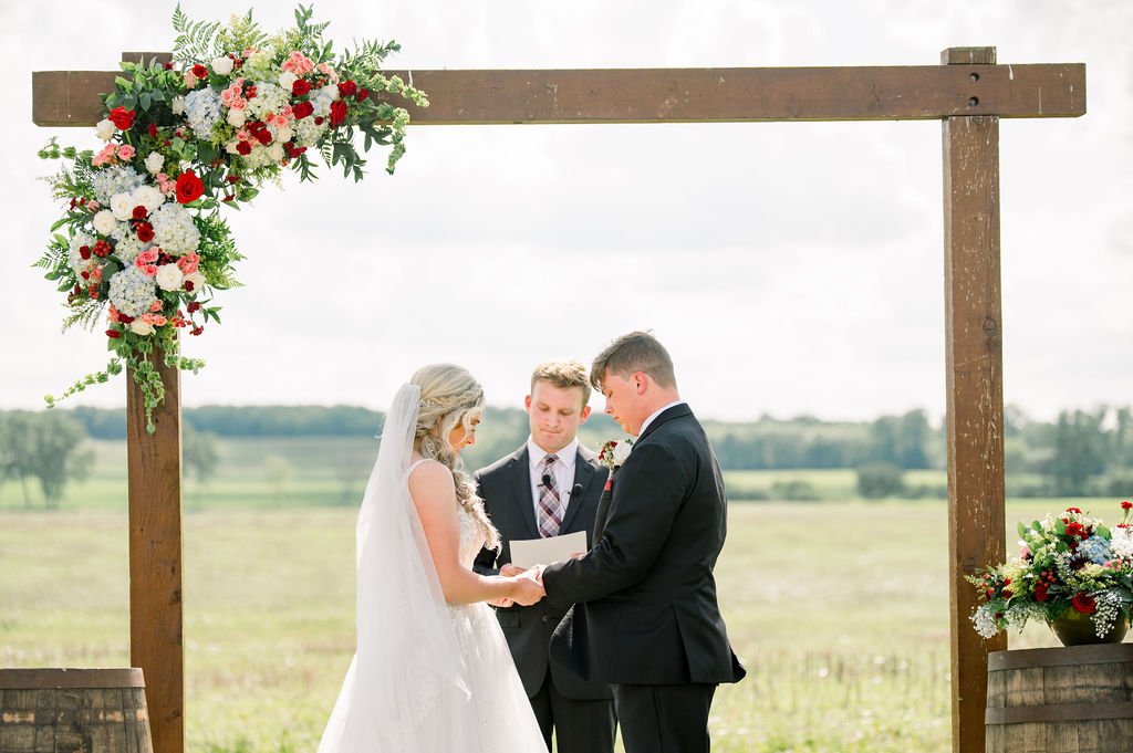 A ceremony arch standing in the open field with guests seated on the grass.