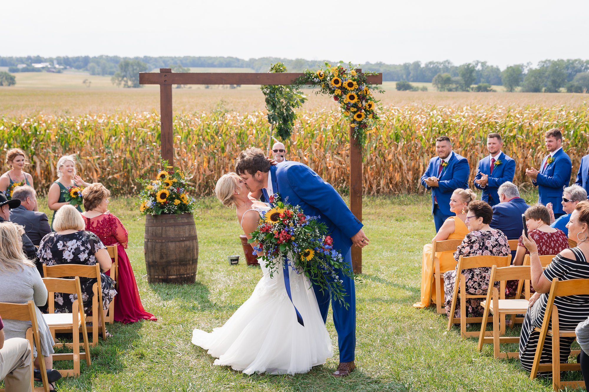 A couple kissing beneath a floral arch by the sunflower field