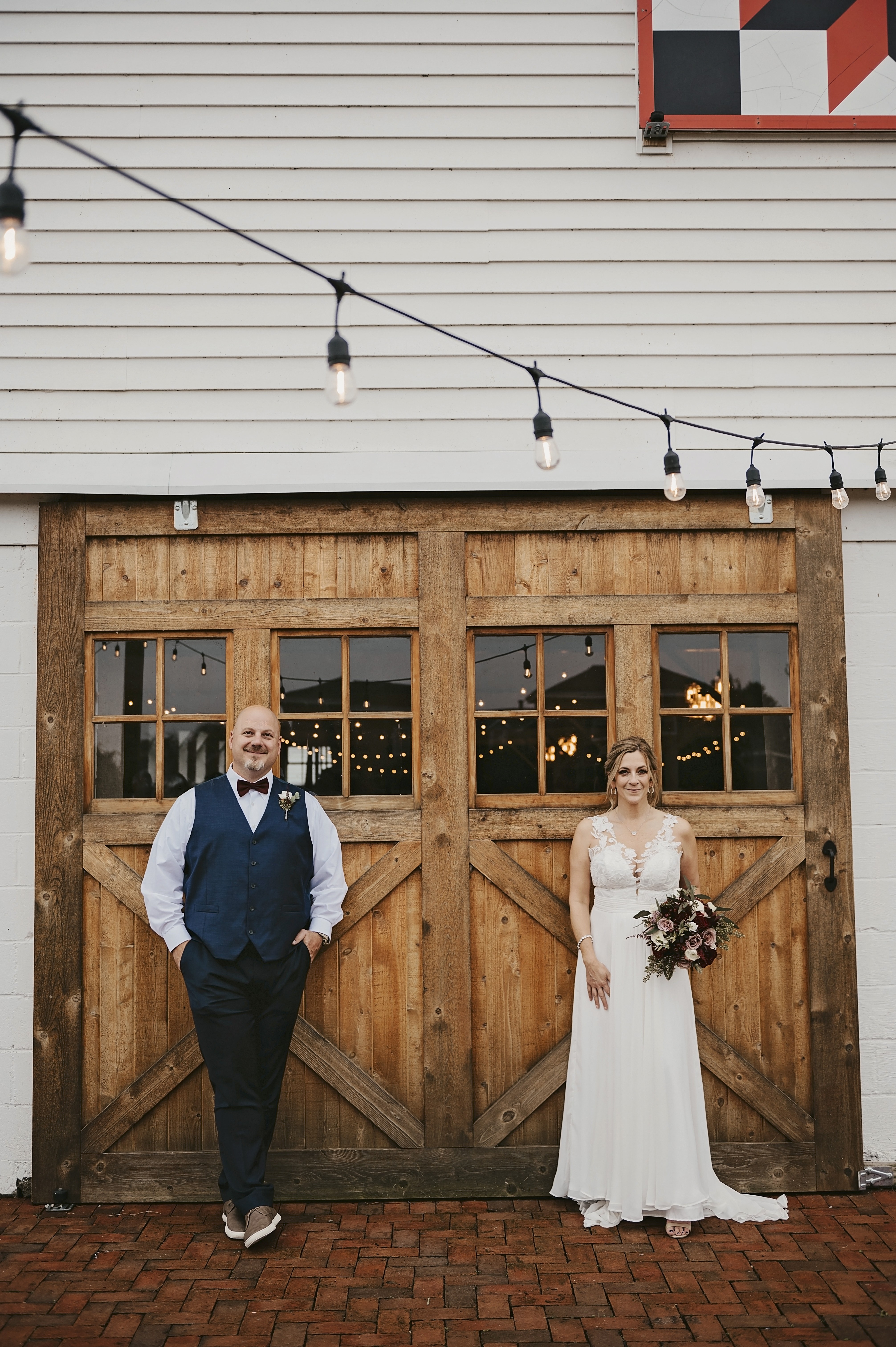 A couple standing either side of the barn doors under the lights.