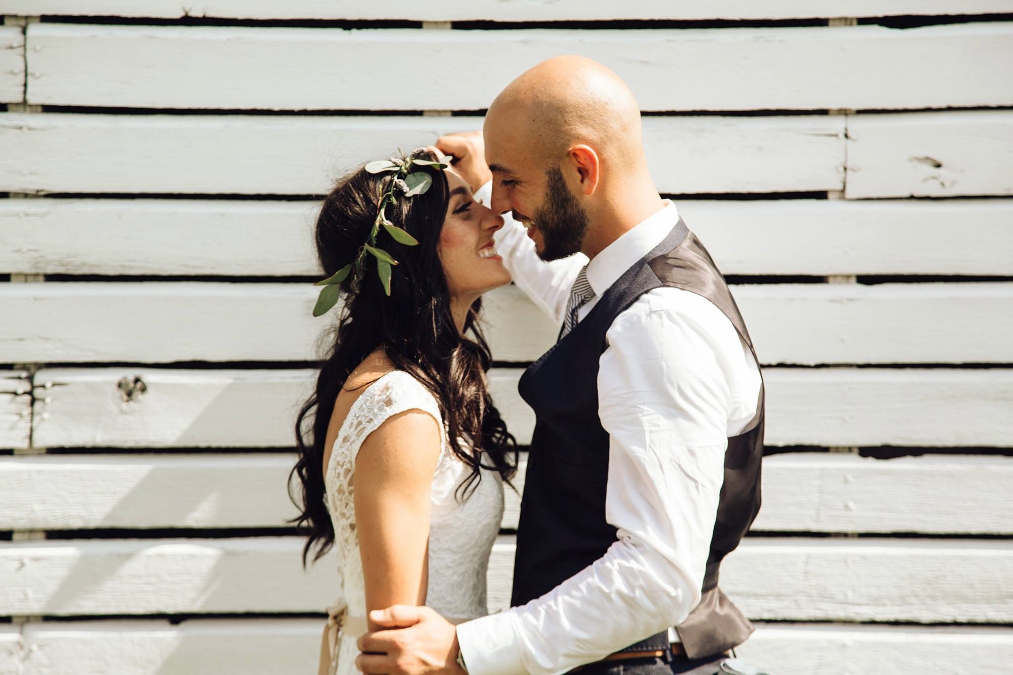 A couple close together against the white barn siding.