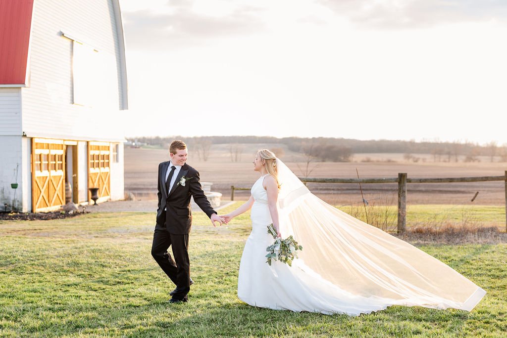 A bride's veil catching the wind beside the barn.