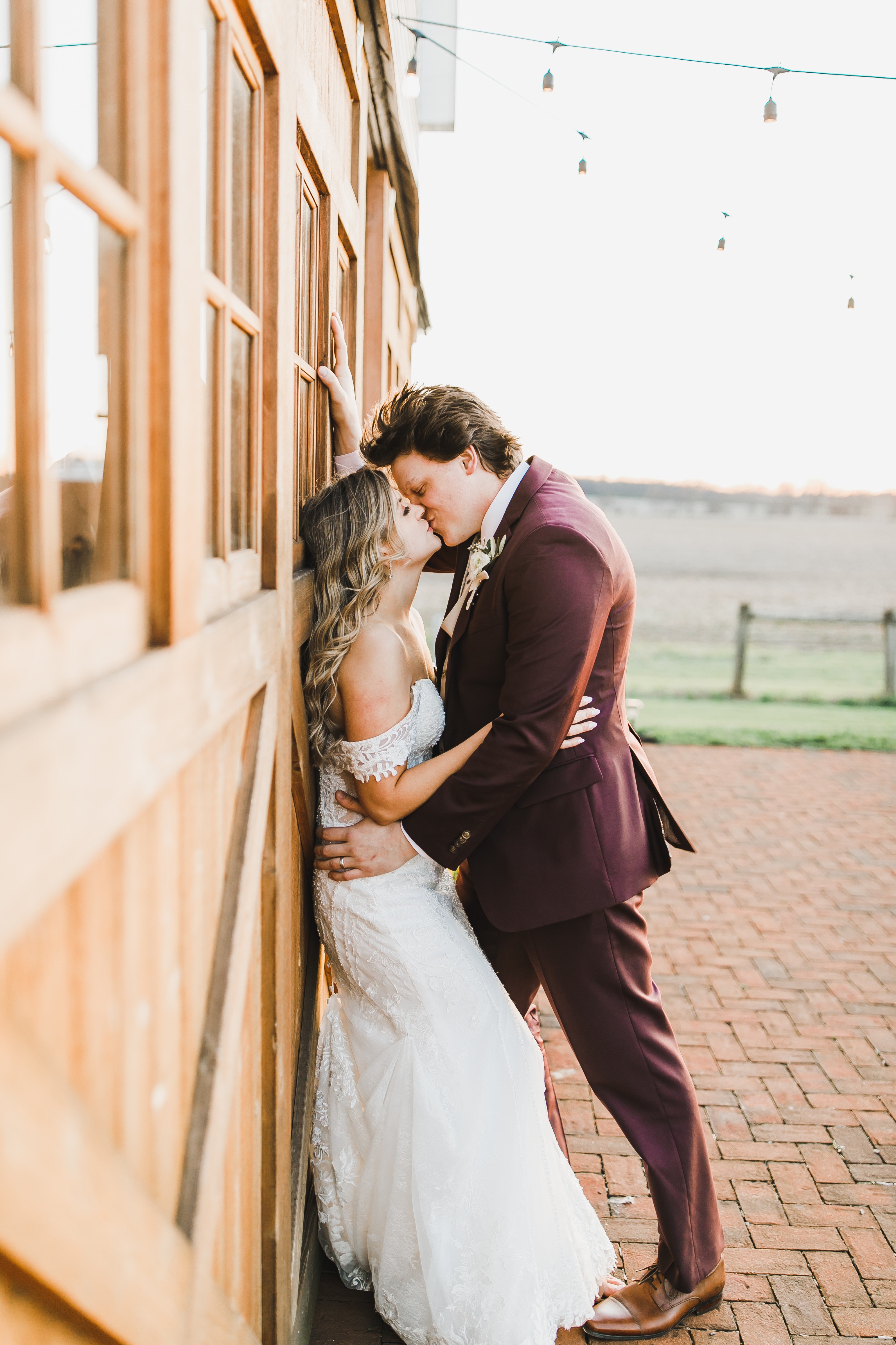 A couple in burgundy and lace against the brick of the farmhouse.