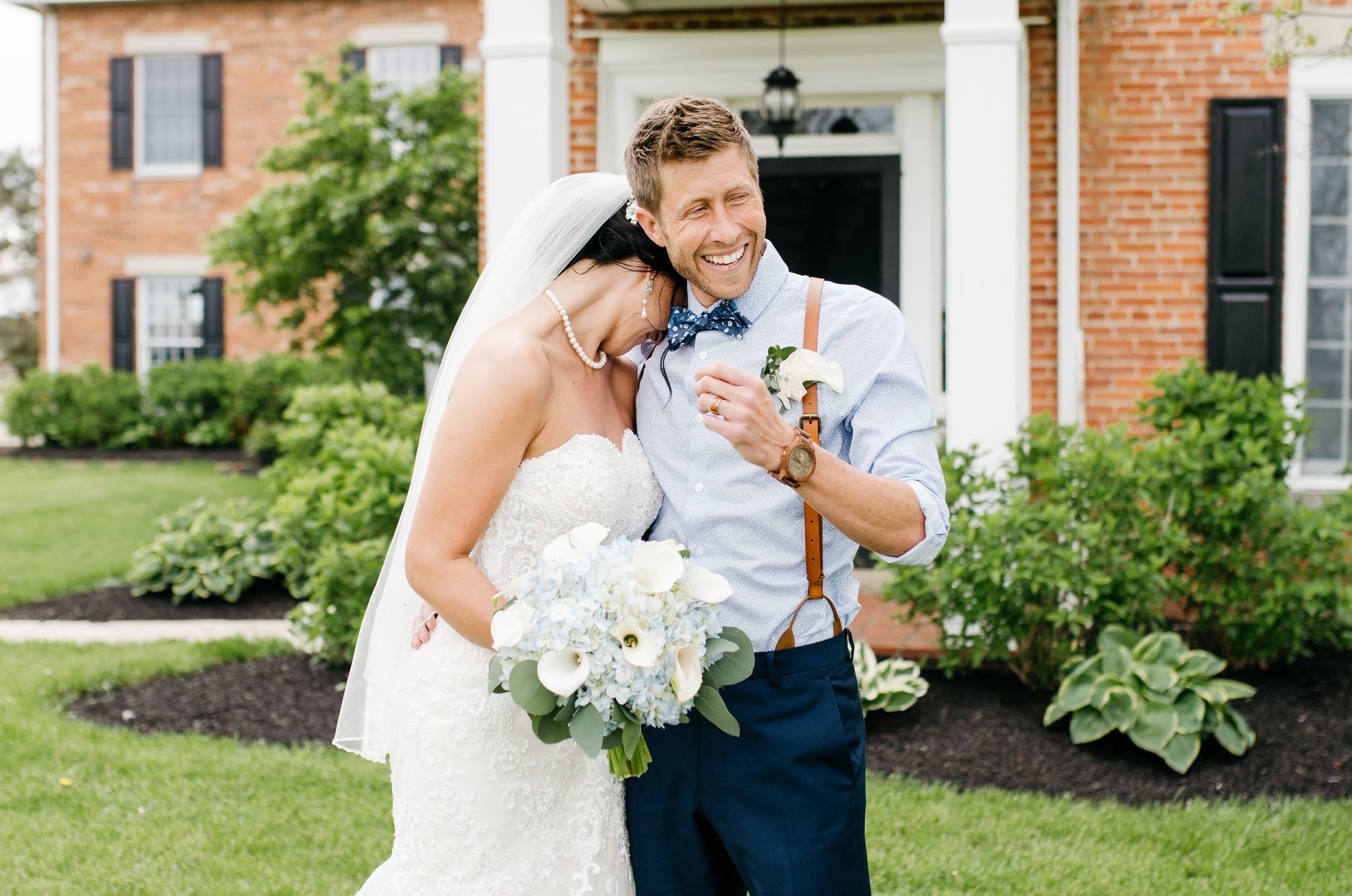 A couple laughing together on the lawn in front of the farmhouse.