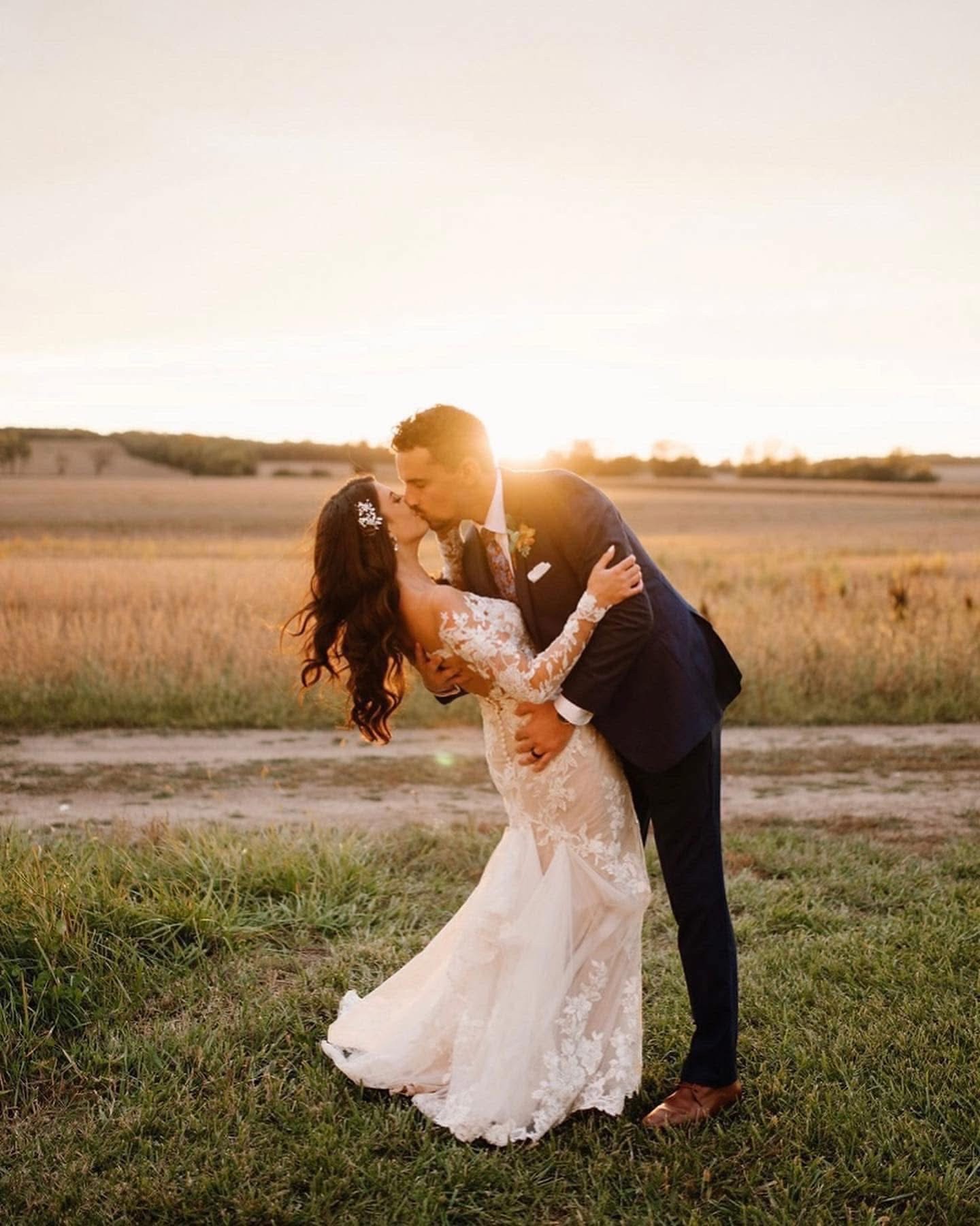 A couple kissing in the field as the sun drops behind them.