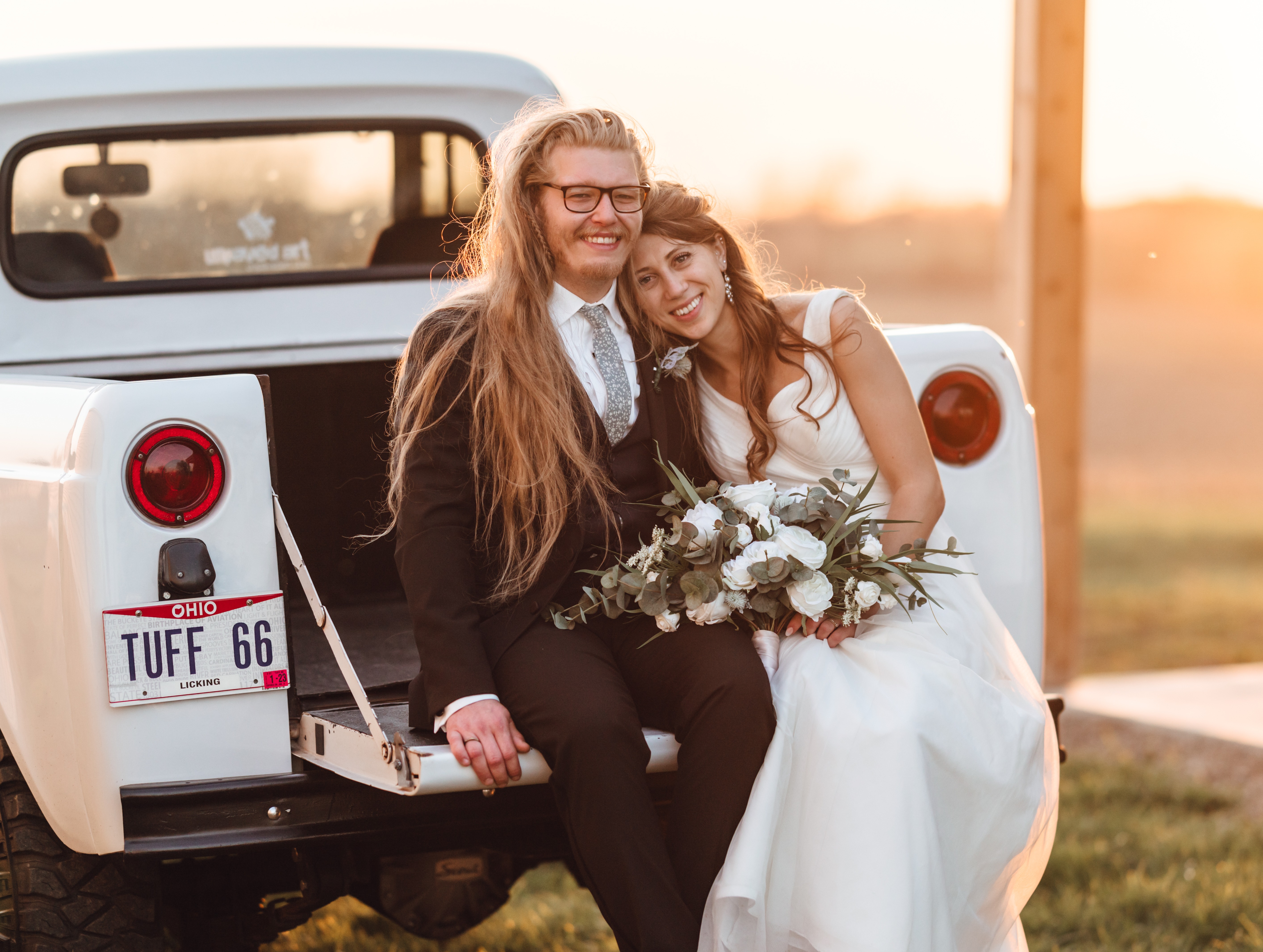 A couple sitting in the back of a vintage pickup in the last of the light.