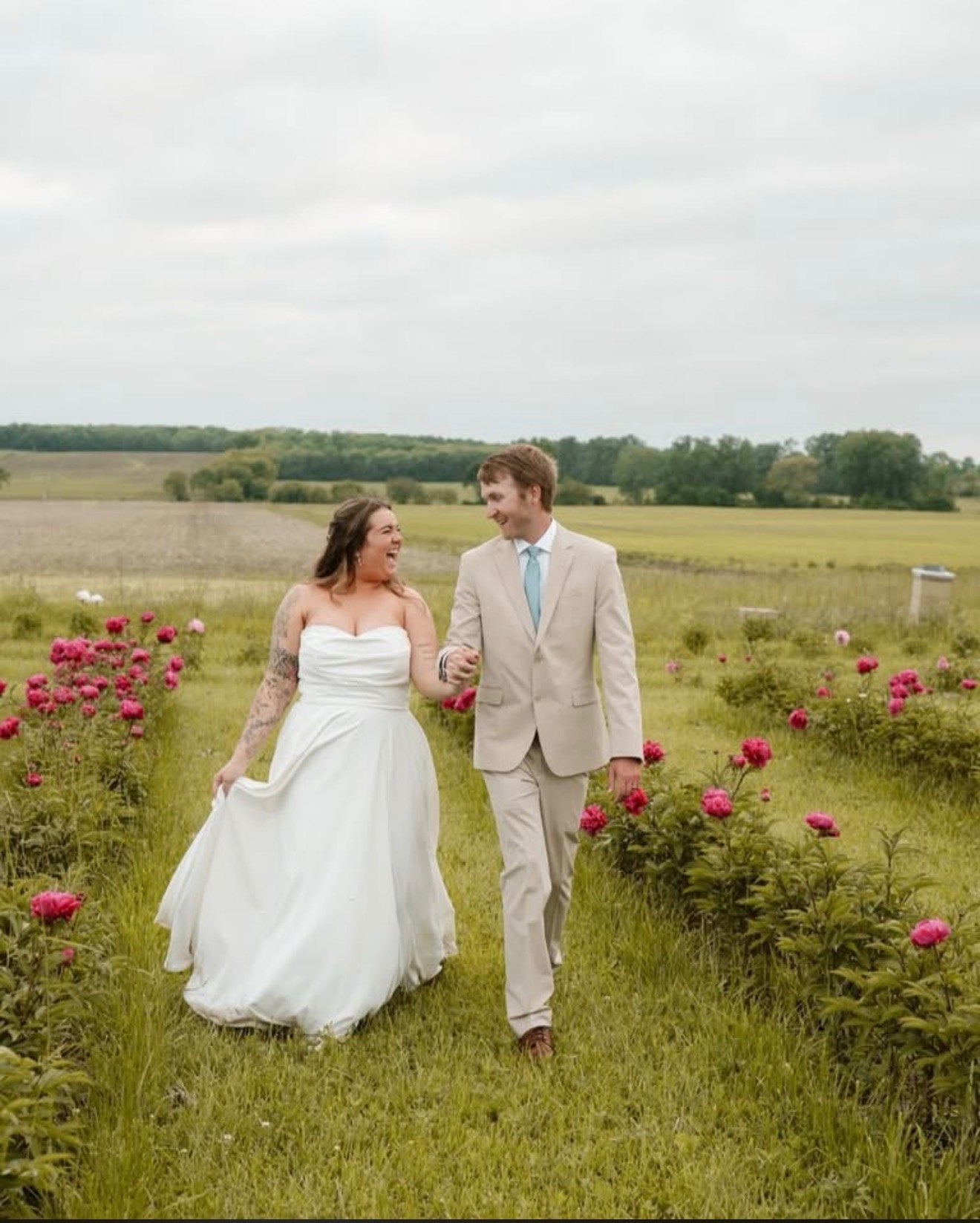 A bride and groom walking hand in hand through the blooming peony rows