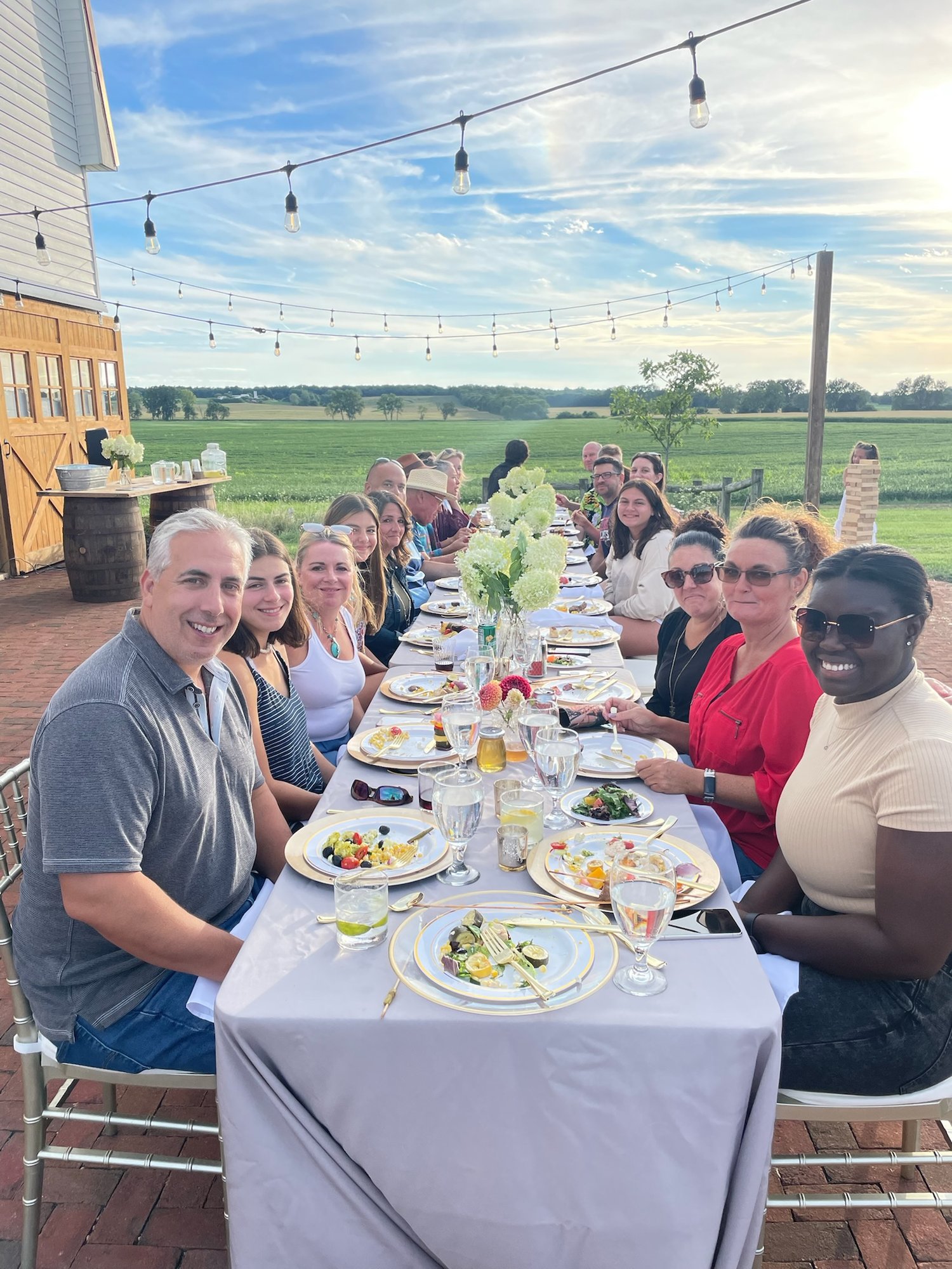 Guests share a long table on the brick patio at golden hour under string lights.