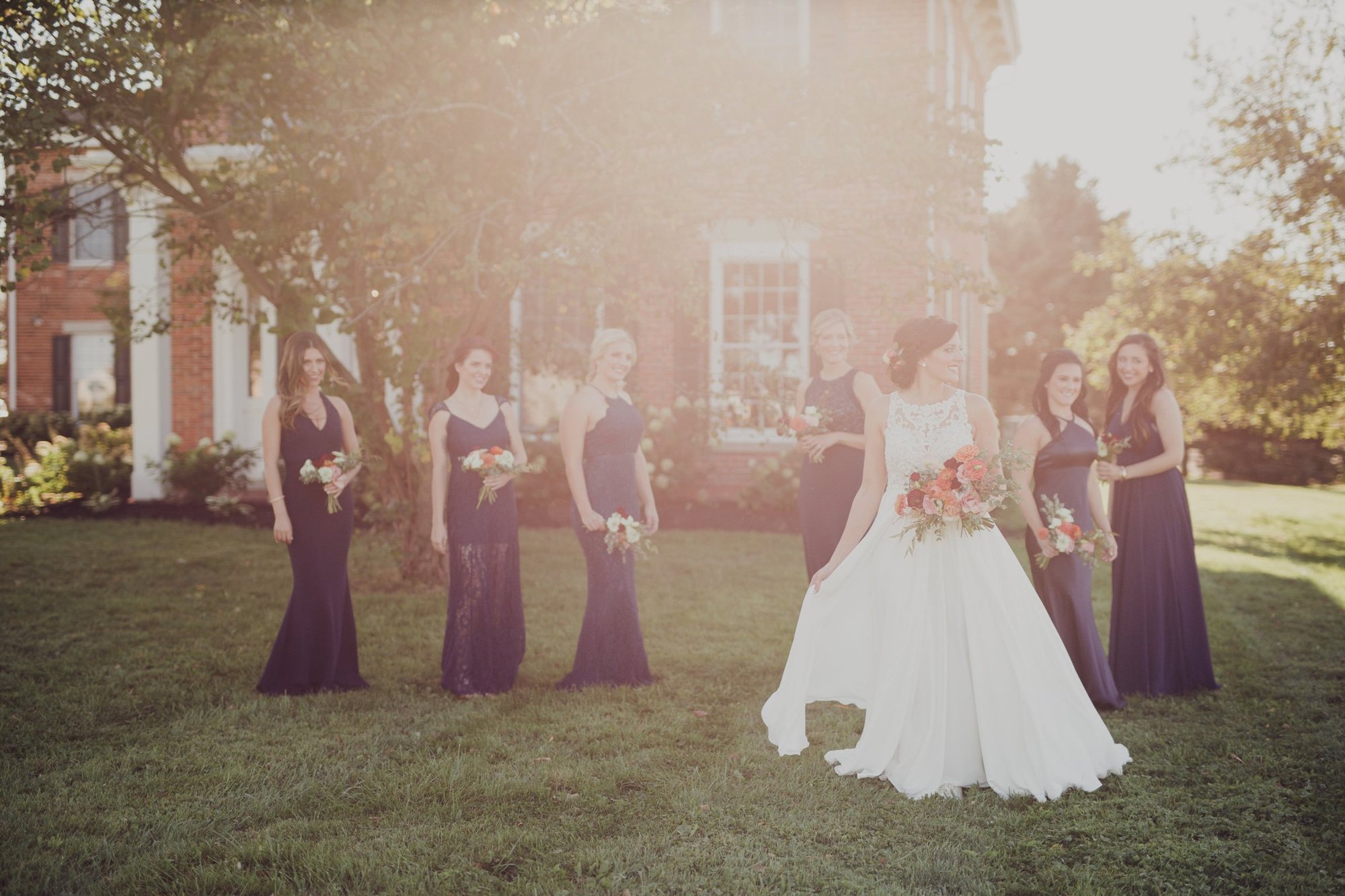 The wedding party in plum gowns gathered at the farmhouse at golden hour.