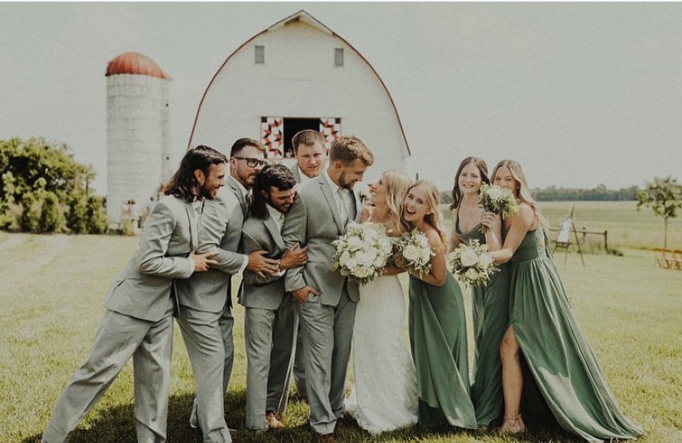 The full wedding party in sage and grey gathered beside the silo.