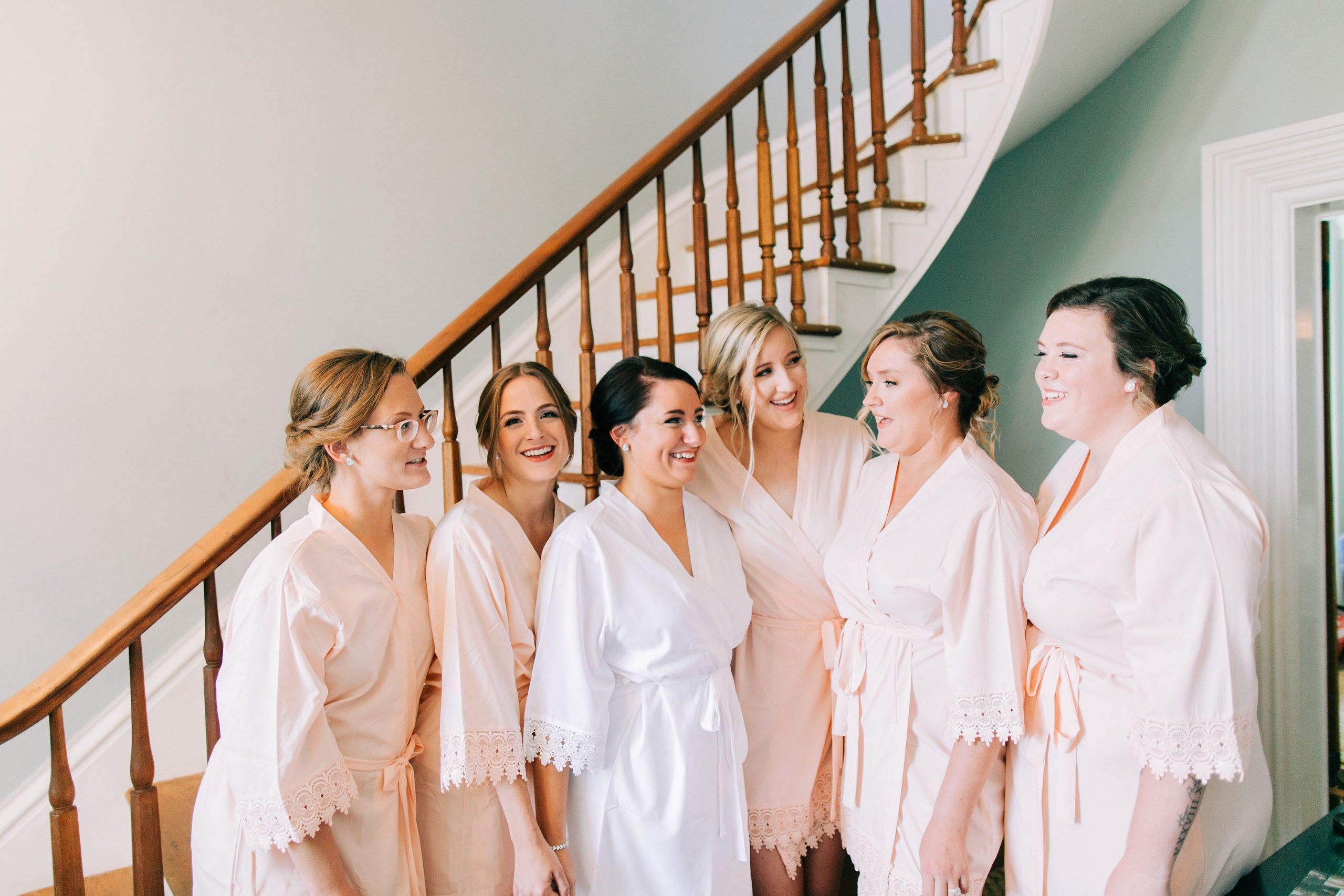 The bride and her attendants in matching robes at the foot of the farmhouse staircase before getting dressed.