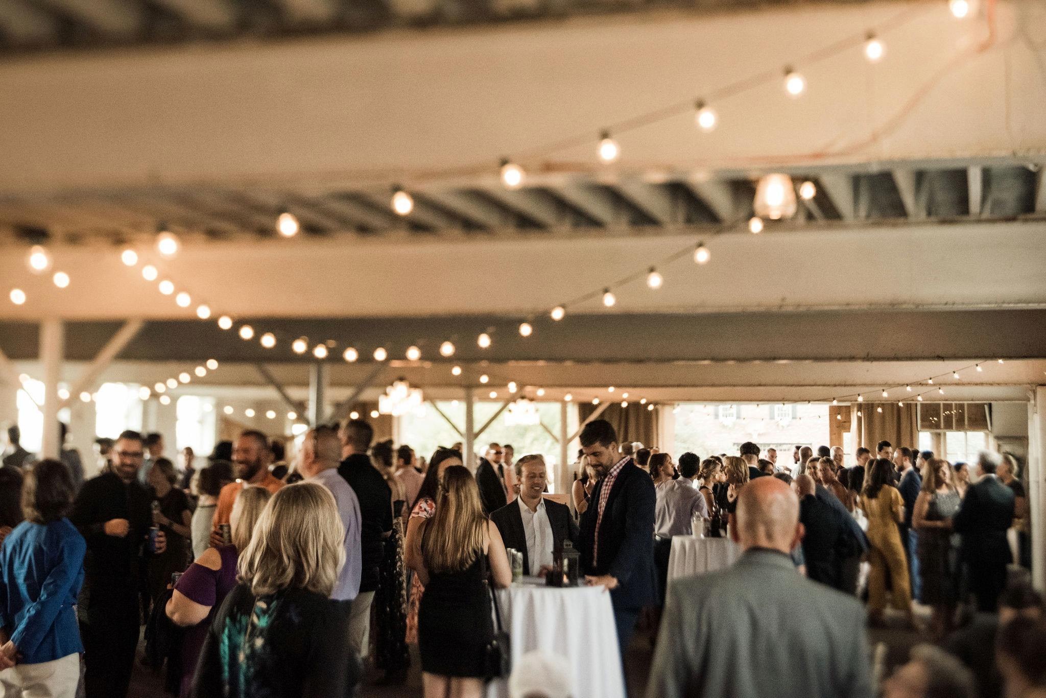 Guests mingle during cocktail hour inside the barn beneath strings of warm lights.