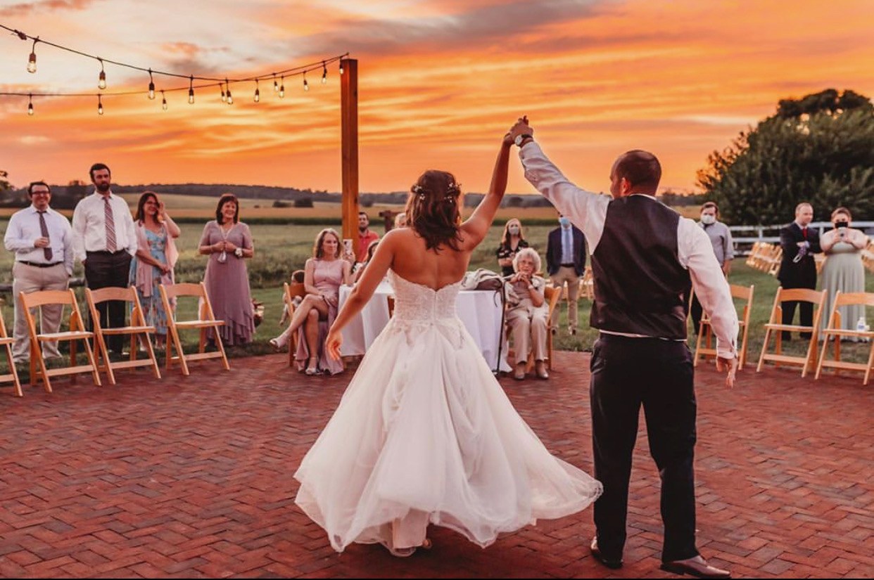 A couple's first dance out on the brick patio, guests watching, the sky orange behind them.