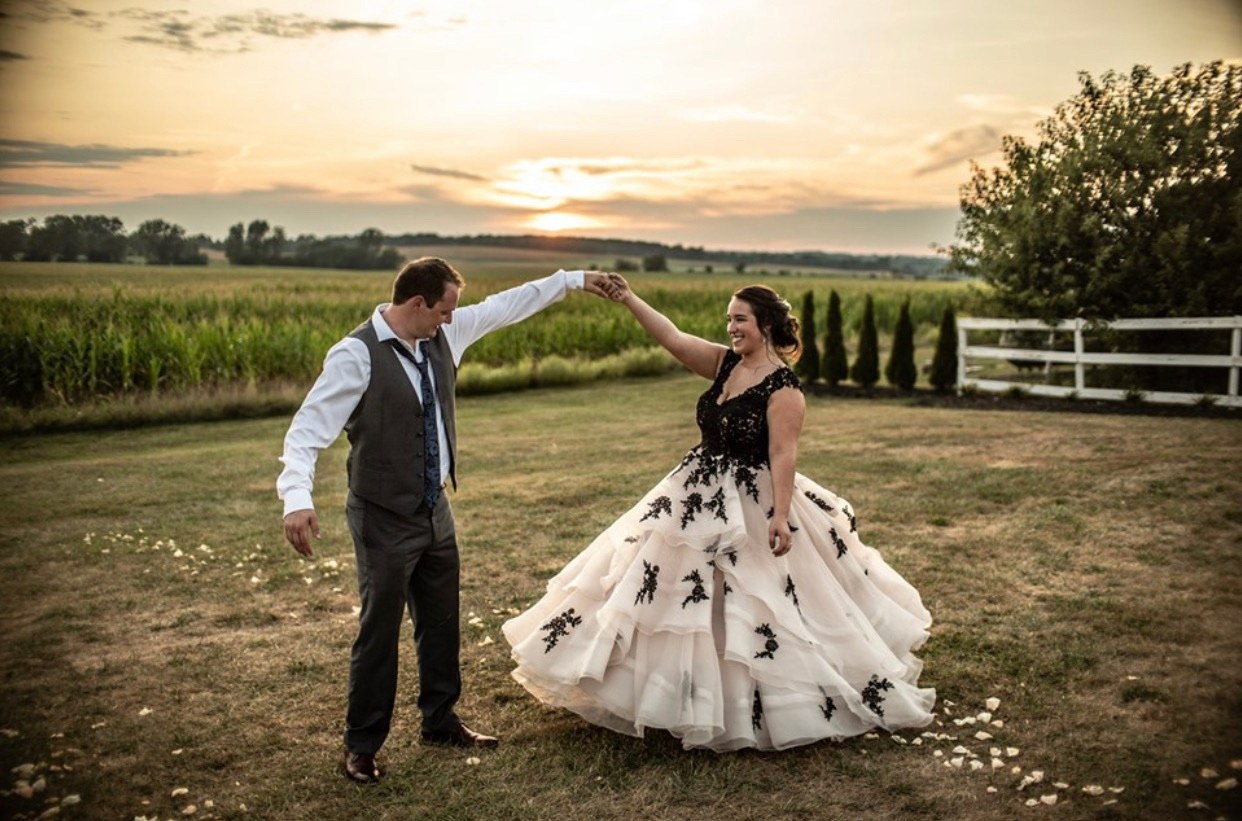 A newlywed couple turns together in the open field at sunset.