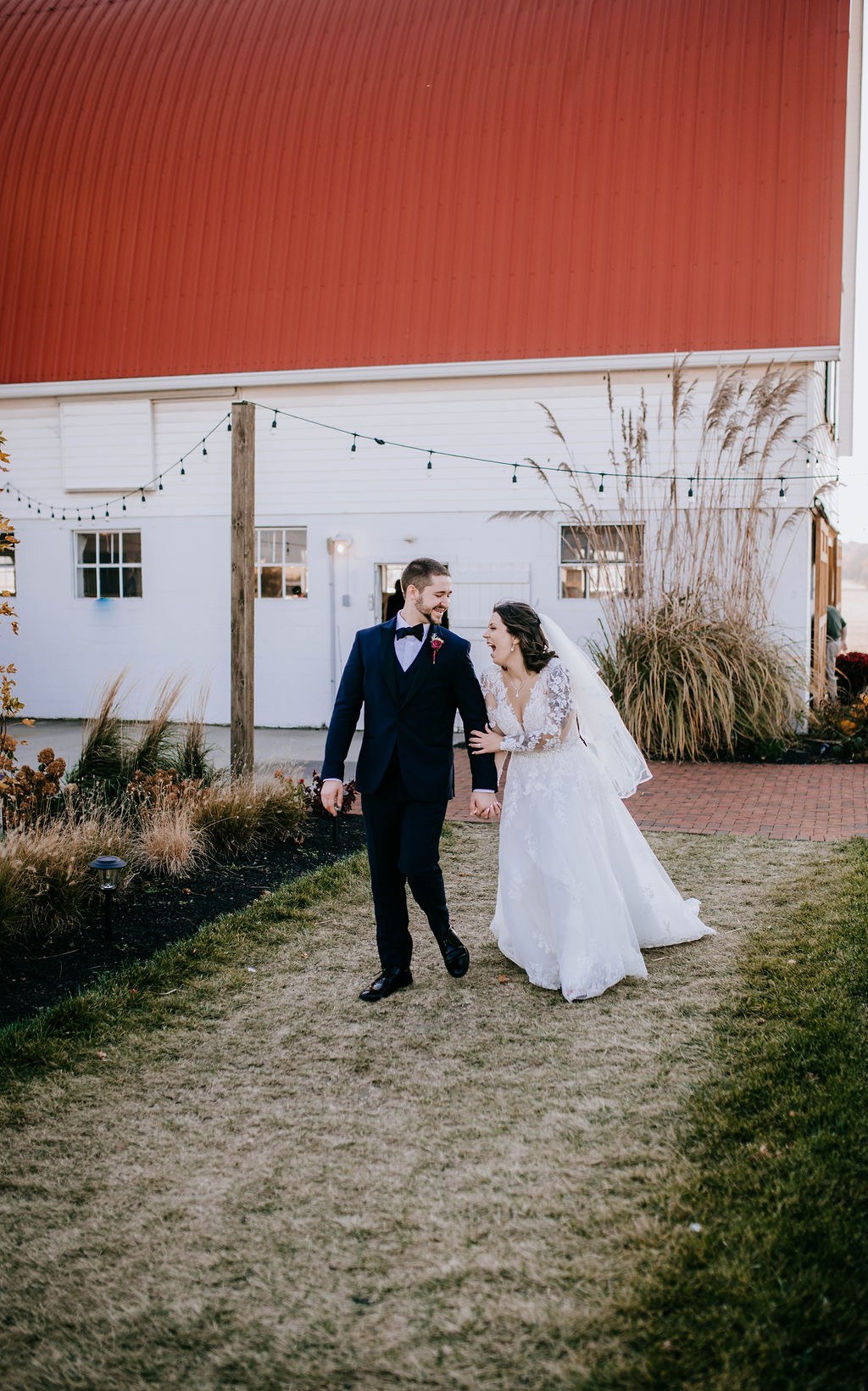 A newlywed couple walks beside the white Wren Farm barn.