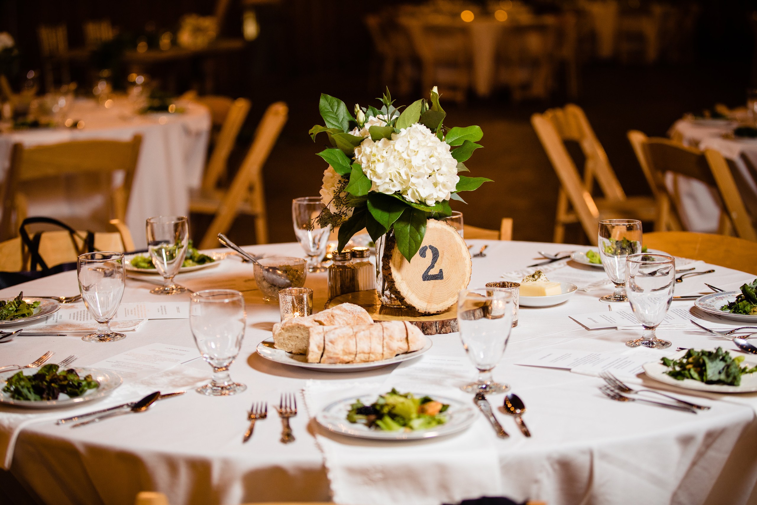 A reception table set with flowers, place settings, and dinner beneath the barn lights.
